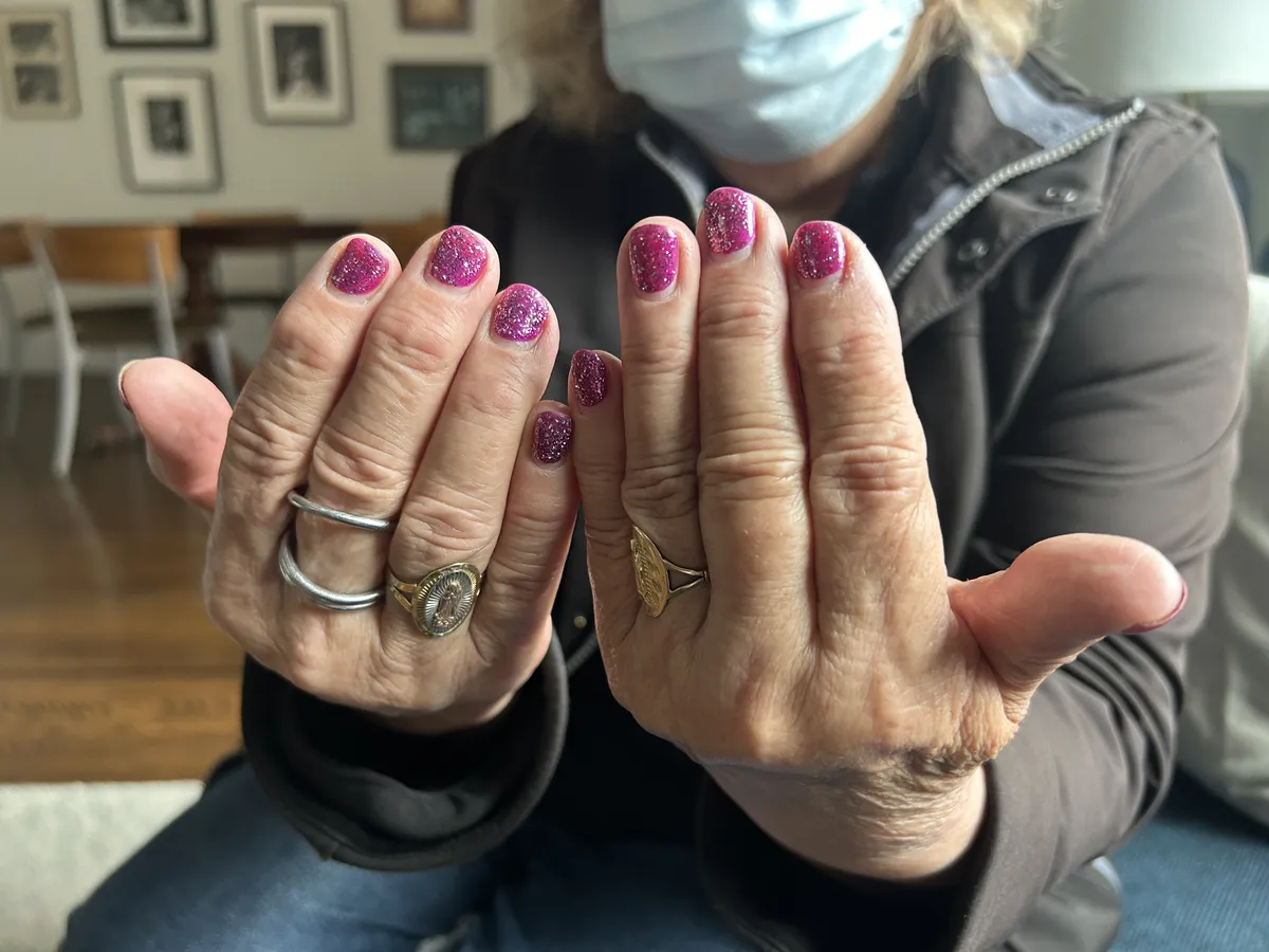 Delia holding up both hands to show off bright pink, sparkly fingernails.