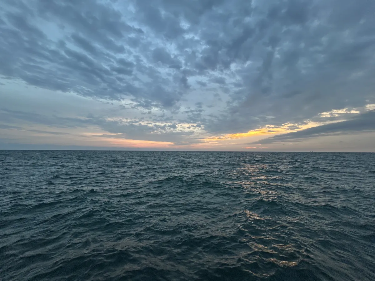 Light peeking out from under clouds, illuminating an expanse of water and sky.