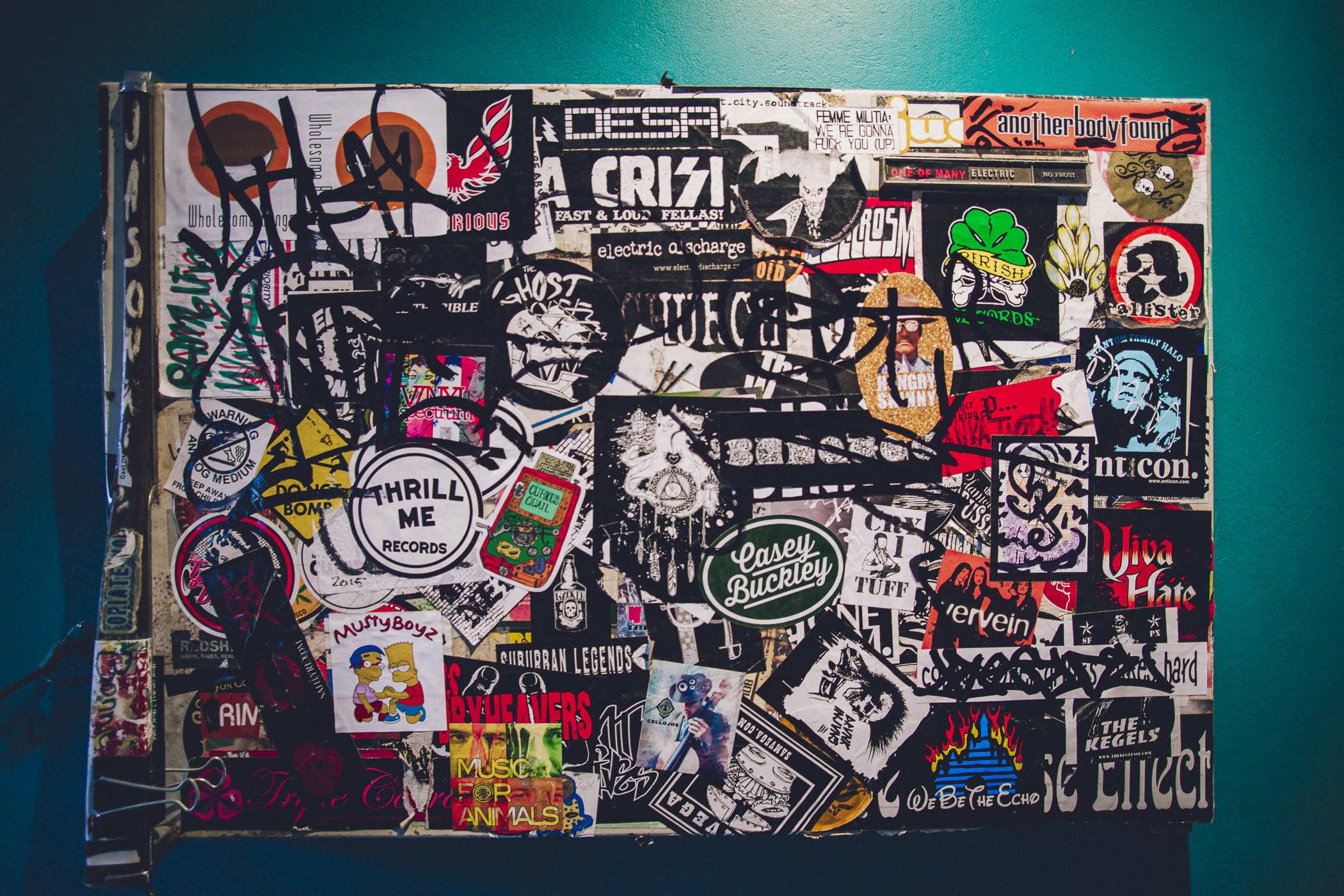 Incomprehensible amalgamation of stickers on a white surface that's been hung on a green wall 