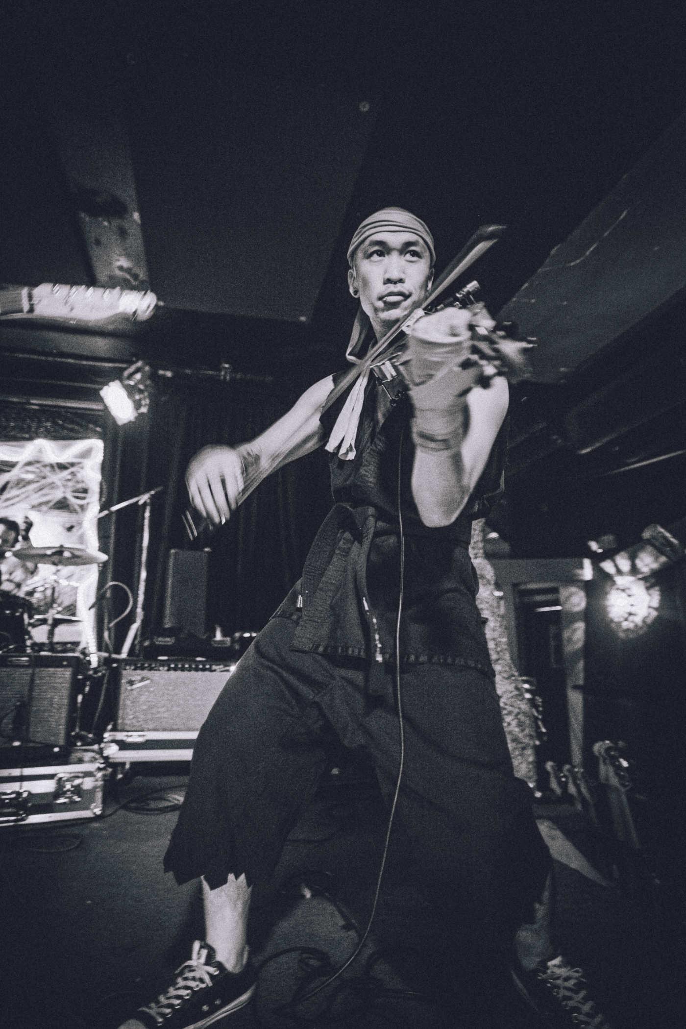 Black and white photo of a man with a shaved head dressed like Ryu from Street Fighter playing the violin