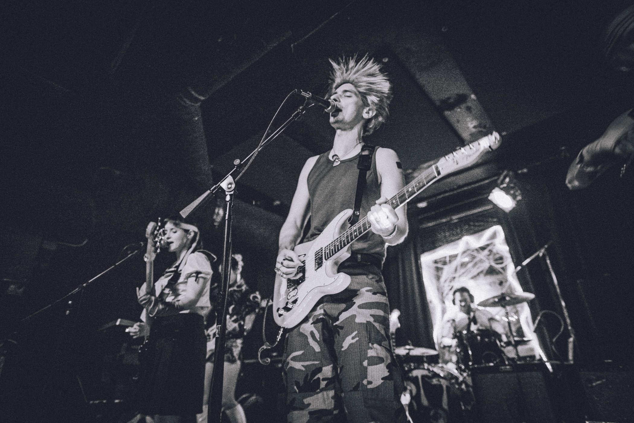 Photo of me playing guitar on stage wearing a tanktop, camo pants and a horrible wig (Guile, from Street Fighter) 