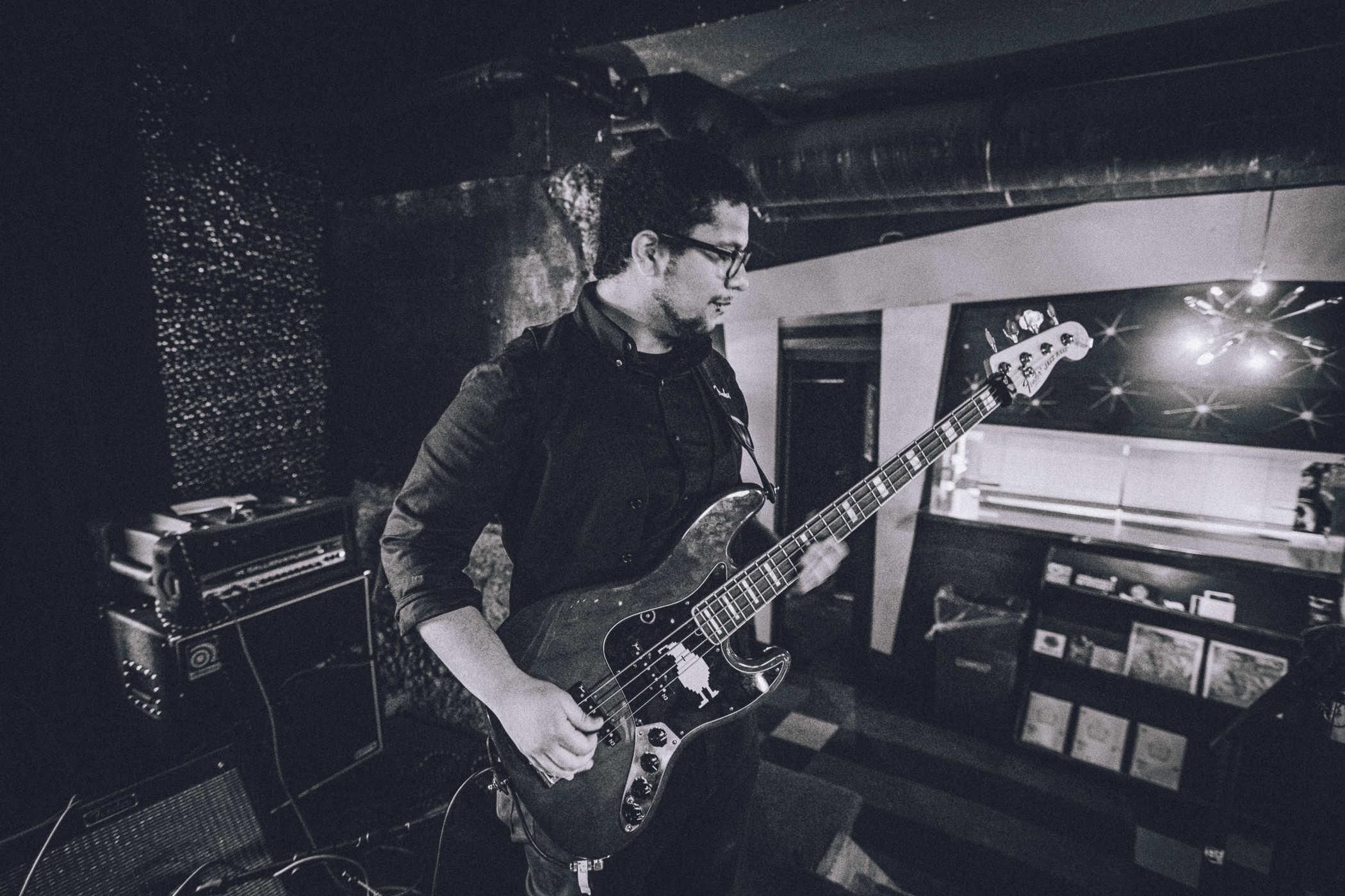 Black and white photo of a person playing bass with a large white quail sticker in the center