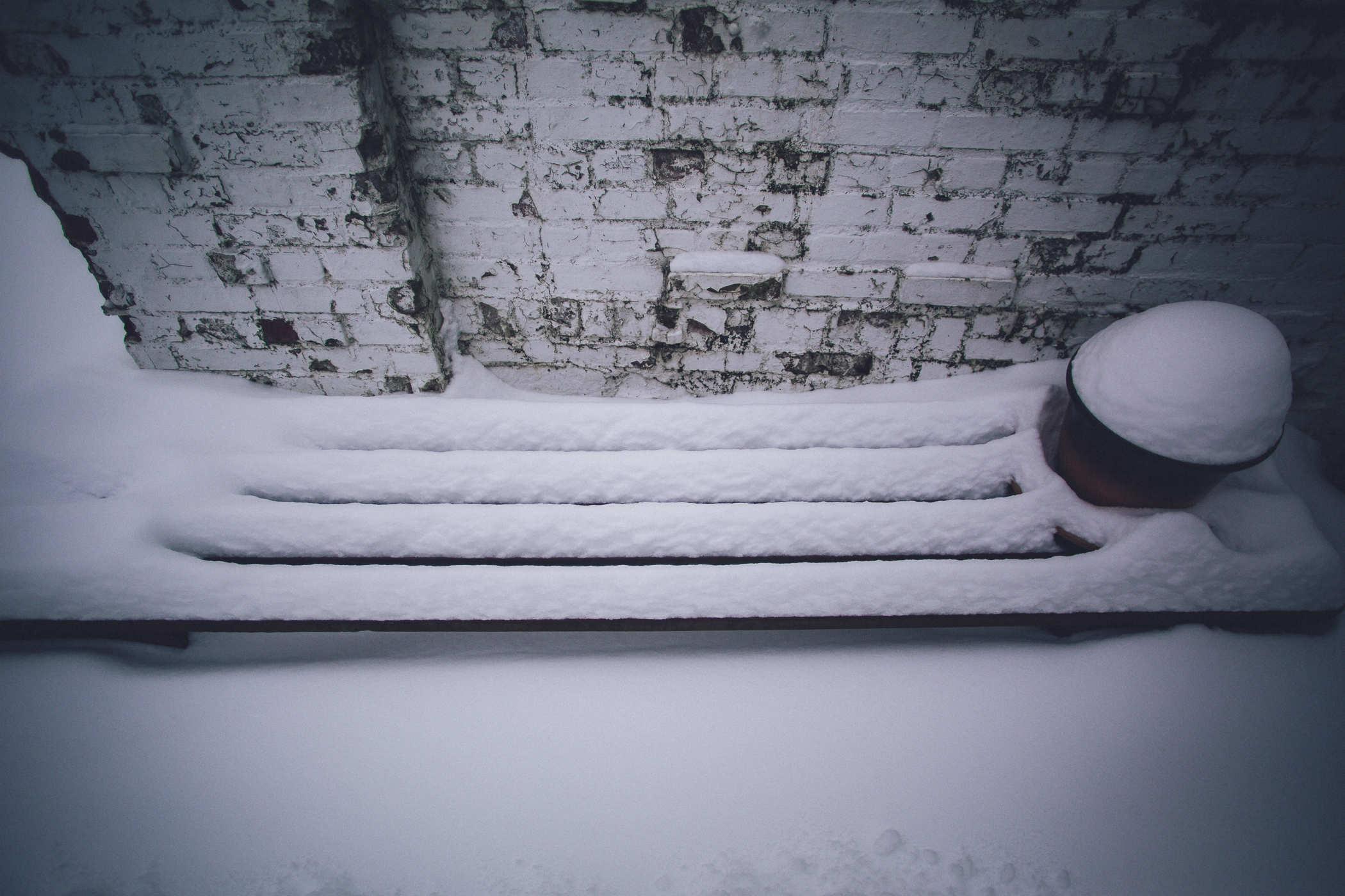 Photo of snow covering a bench next to a white brick wall