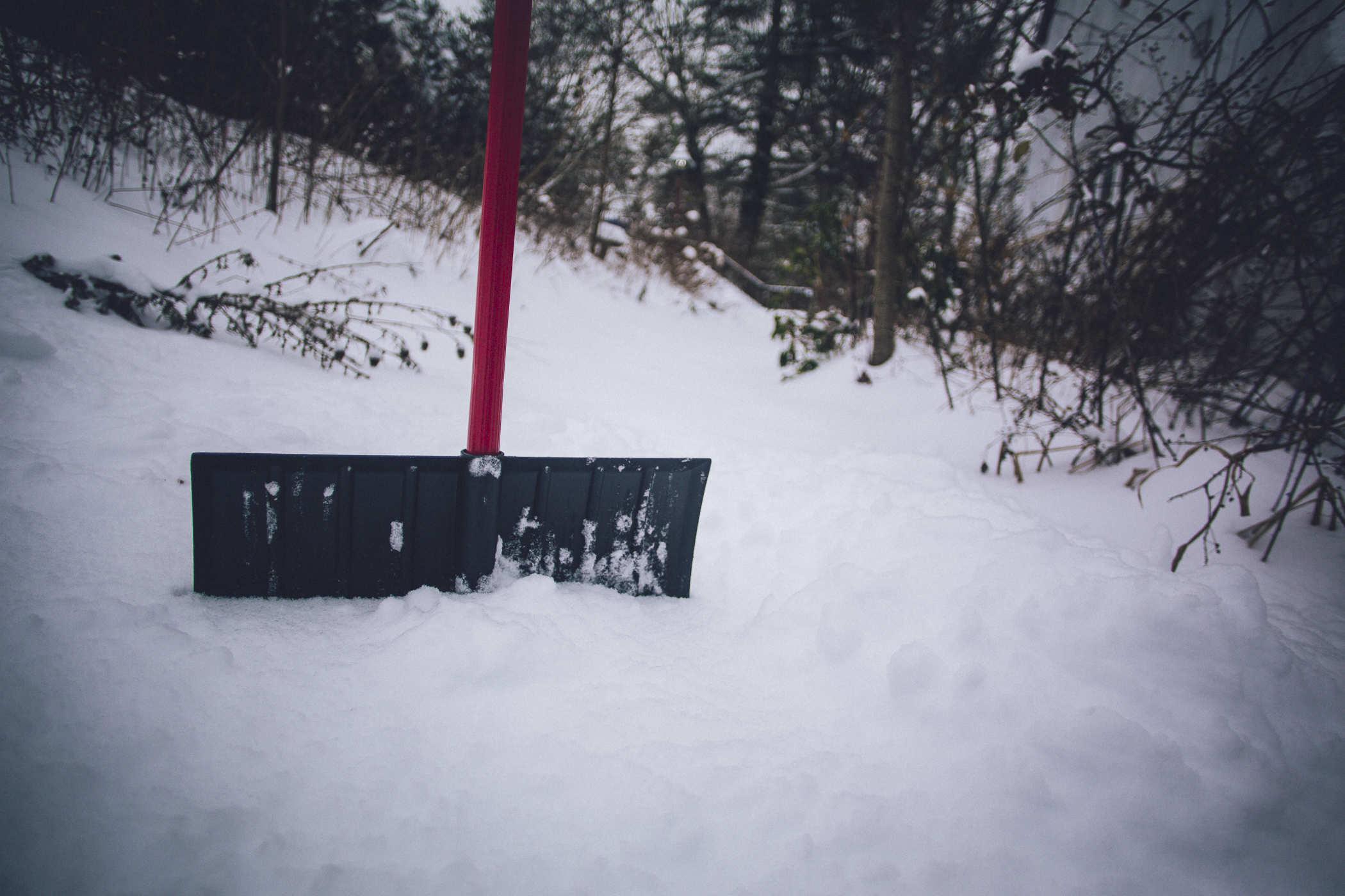 photo of a red handled snow shovel embedded in a thick mound of snow