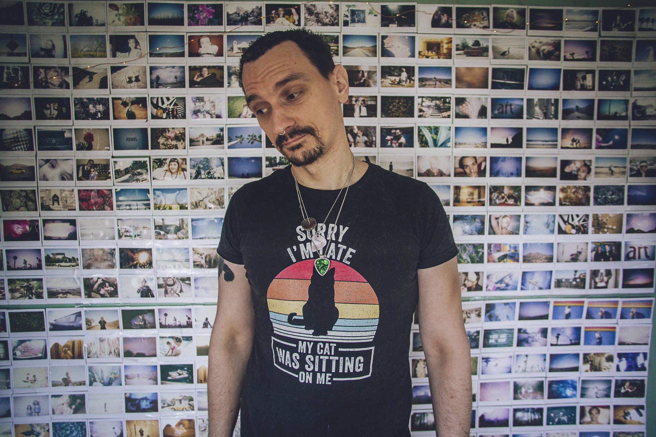 Me in front of the instant film photo wall; I'm wearing a black shirt that says 'SORRY I'M LATE MY CAT WAS SITTING ON ME