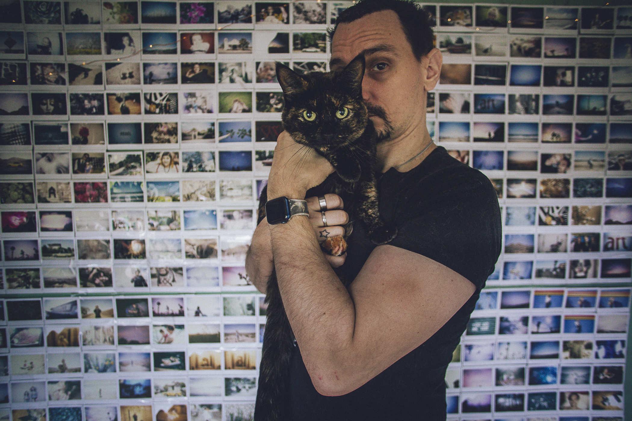 Photo of me in front of the instant film wall holding up a small tortie cat