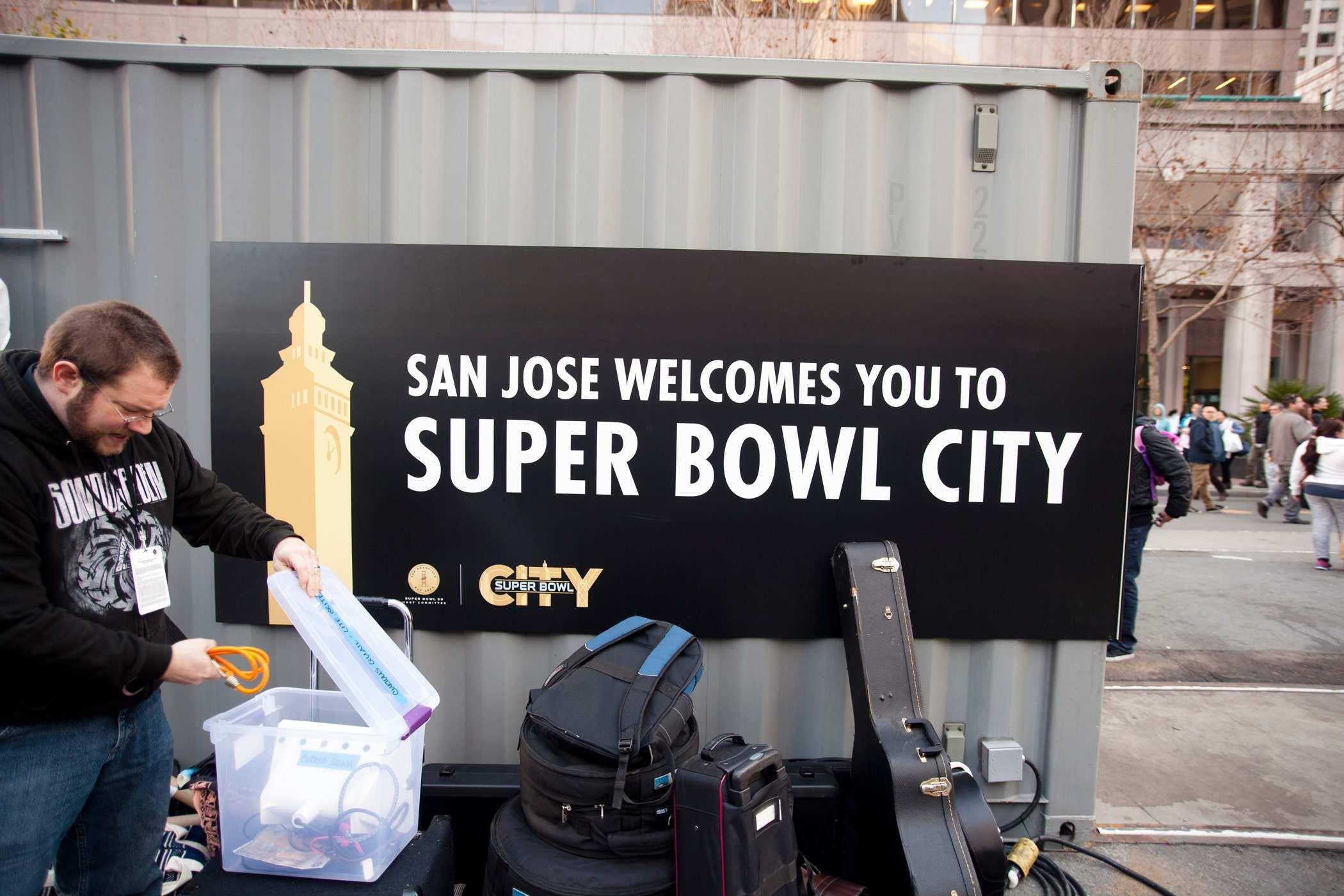 A person unpacking gear behind a large storage unit with a 'SAN JOSE WELCOMES YOU TO SUPER BOWL CITY