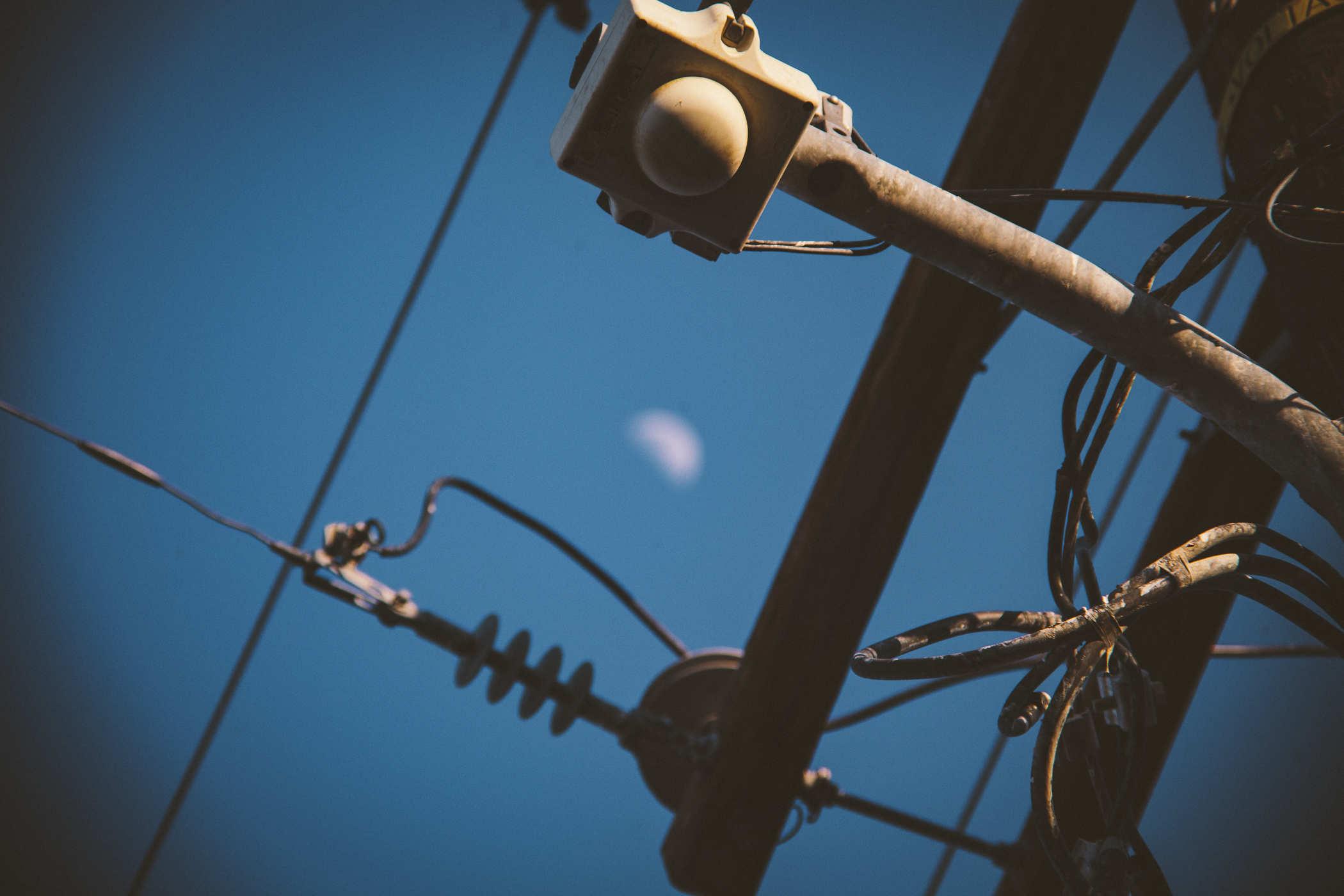 Photo of a utility pole tangled nest of wires with the moon in the background