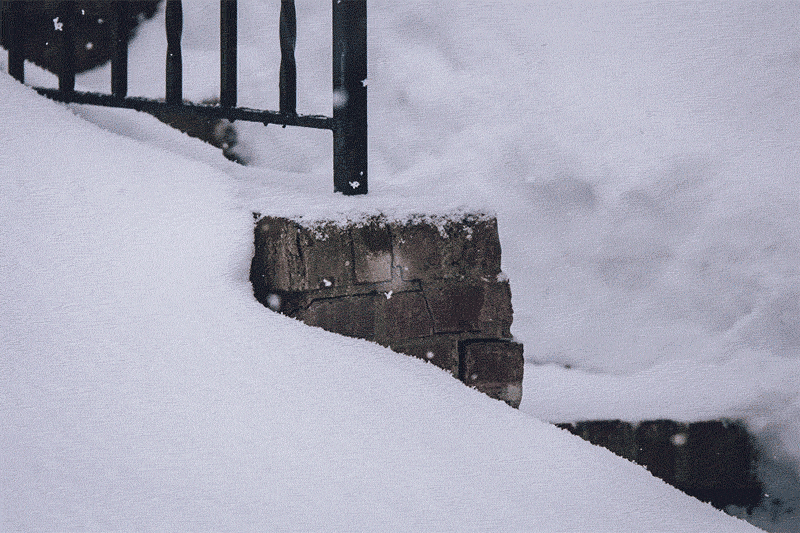Gif of snow falling on a brick staircase with black iron railing 