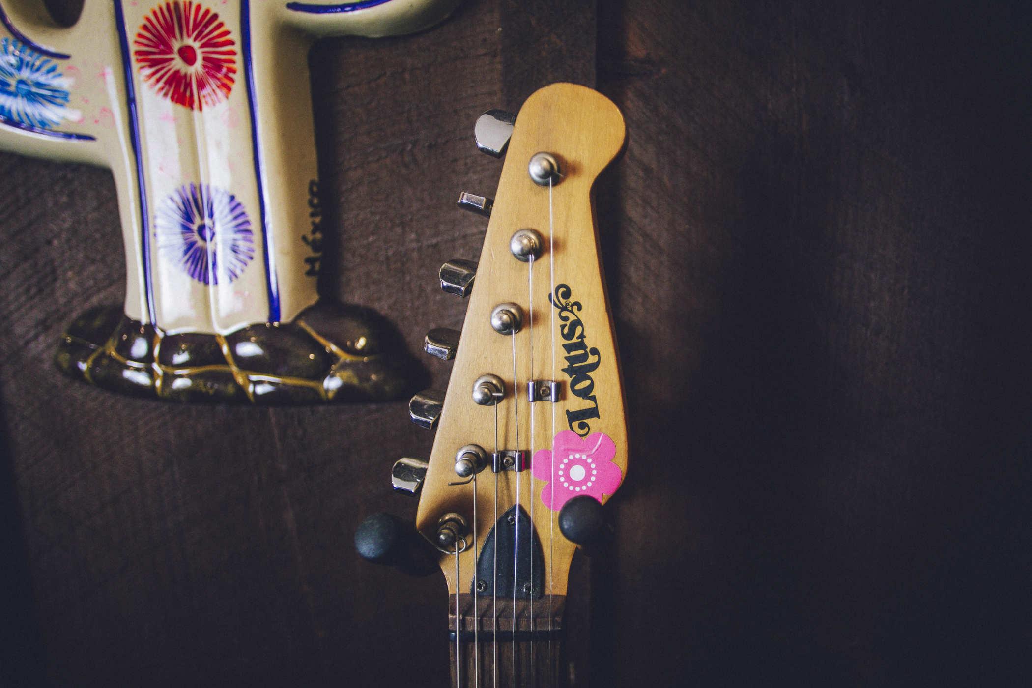 The headstock of the guitar; it reads "Lotus" and has a pink flower sticker on it