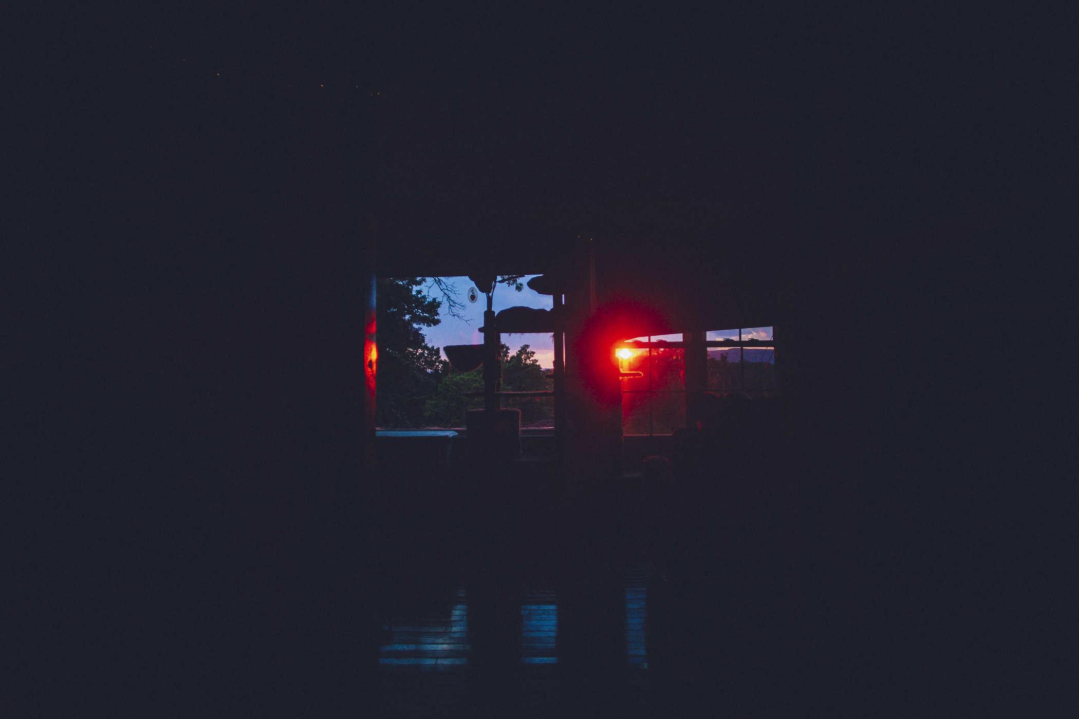 Mostly dark photo of a distance bright red sunset and a cat mansion in silhouette