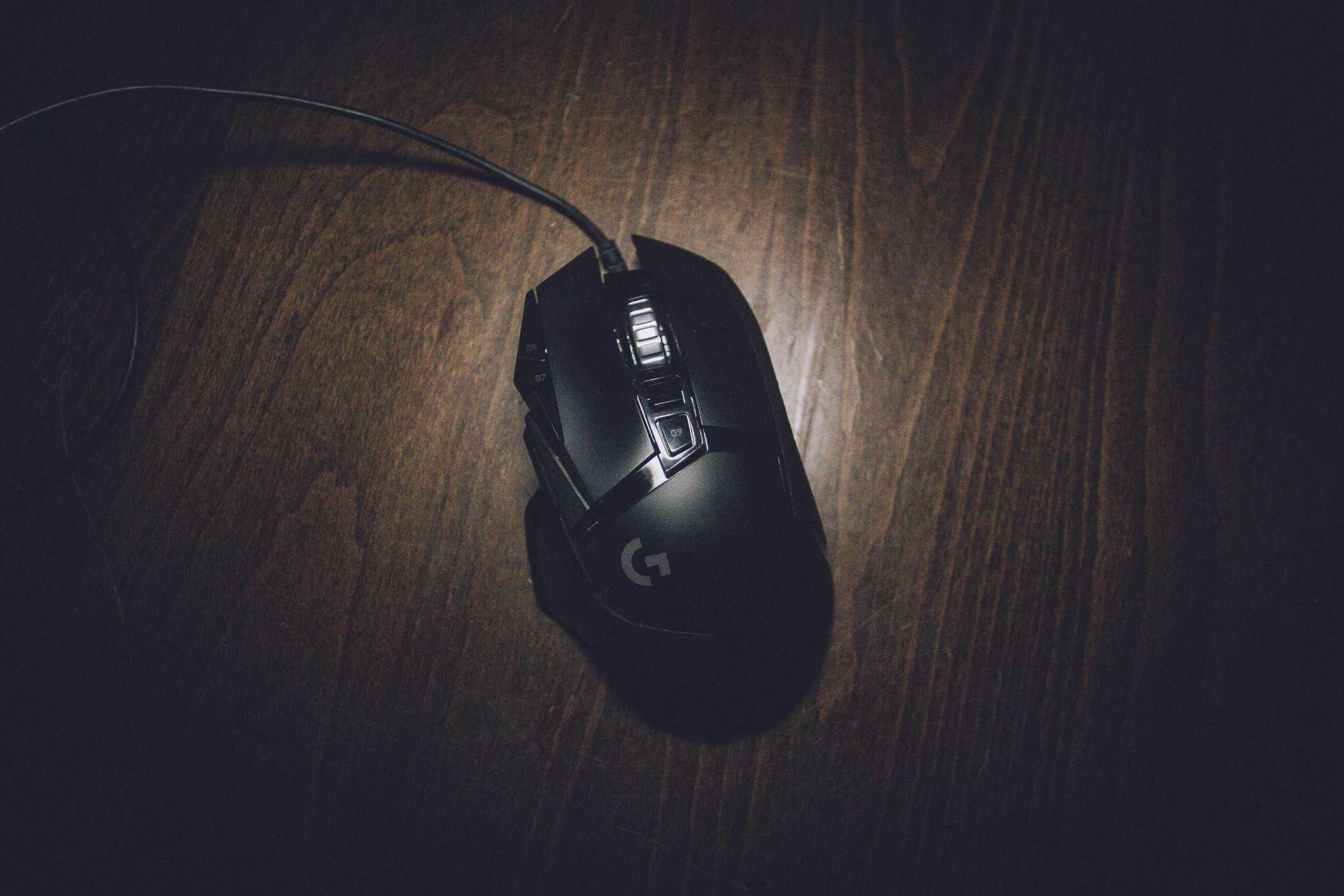 Phot of a black computer mouse on a wooden surface; the mouse has a letter G on it