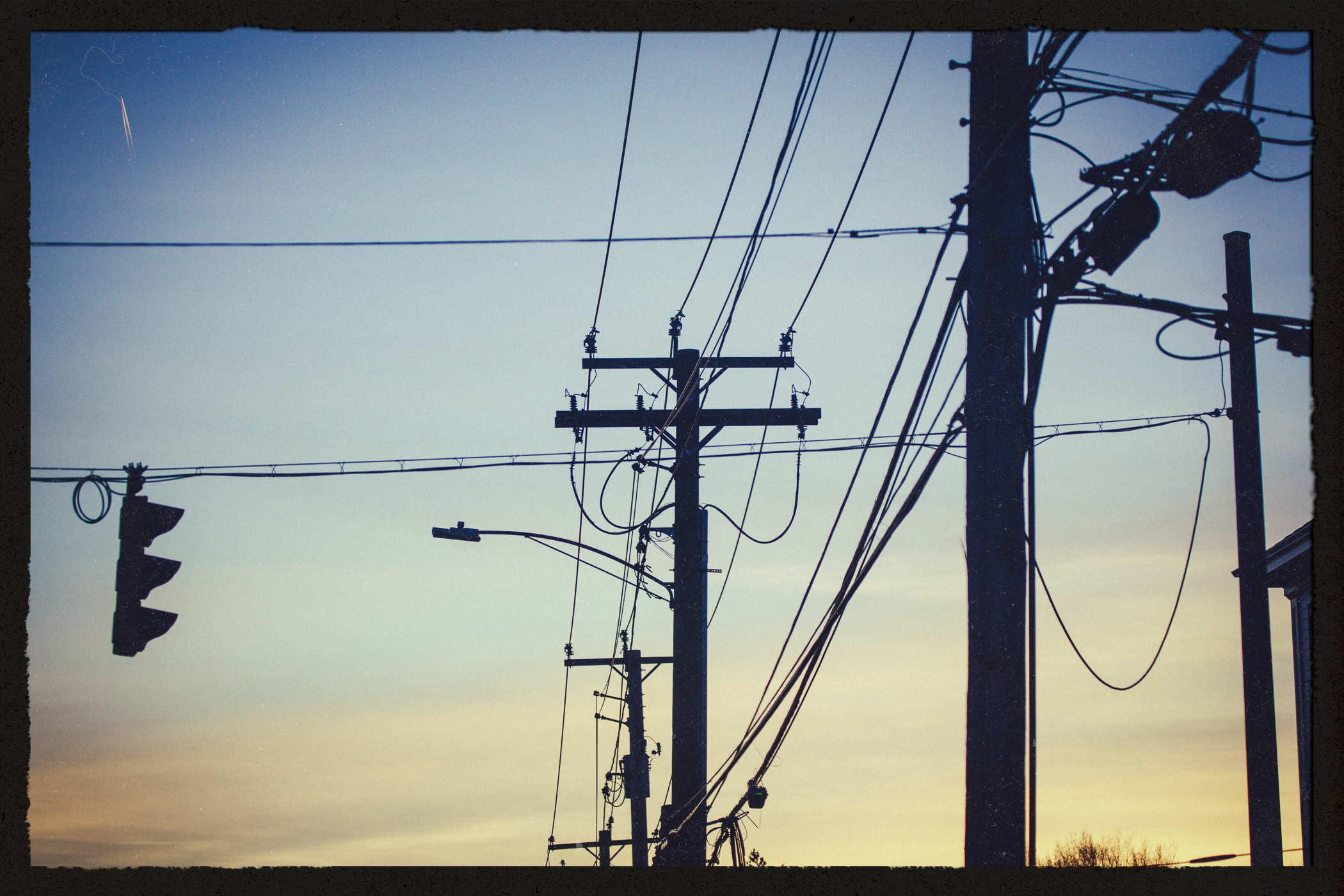 Photo of a bunch of power lines and utility poles in silhouette on a sunset backdrop