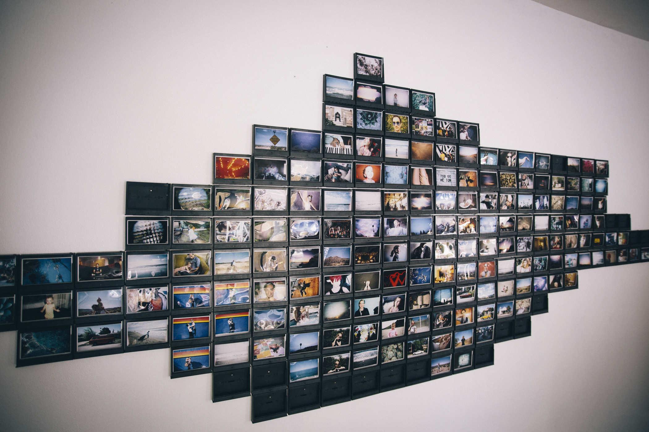 Photo of a long white wall with black rectangles being arranged in it; some of them have photos in them