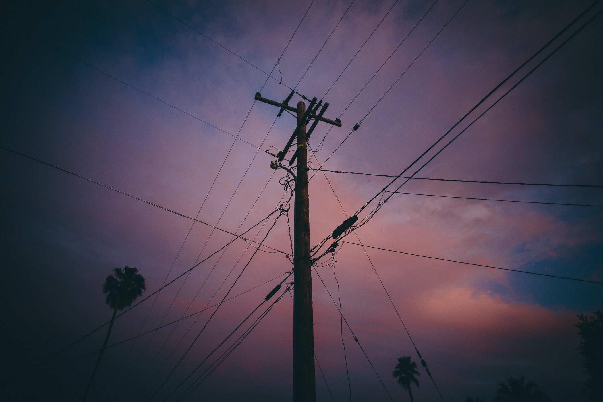 Photo of bisexual colored sky with a large utility pole surrounded by power lines in the center