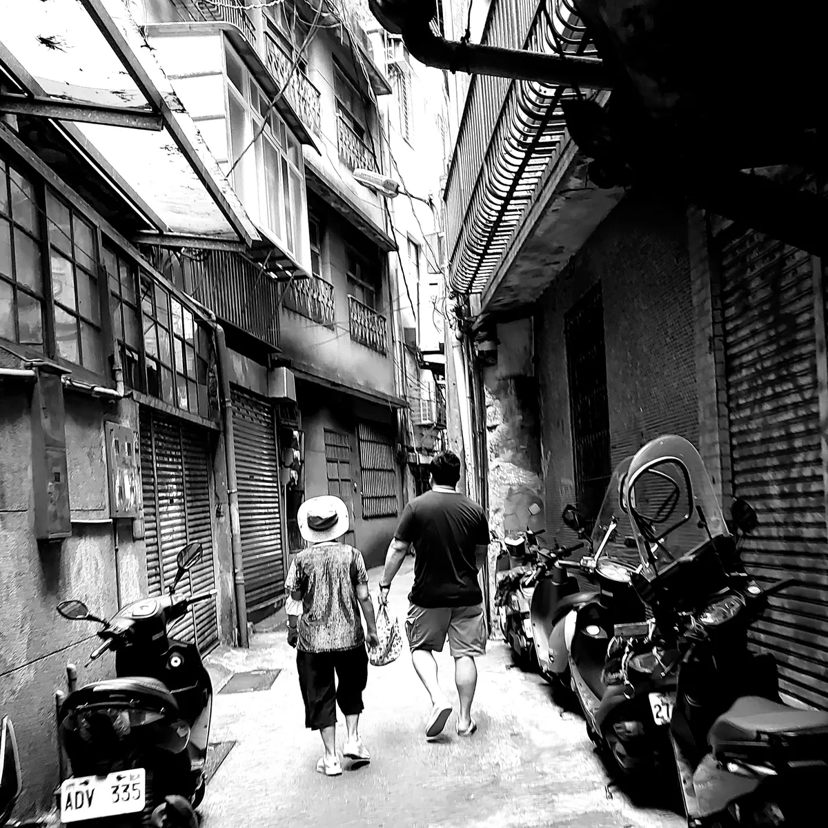 Man helping an old woman carry her bag through a covered alleyway