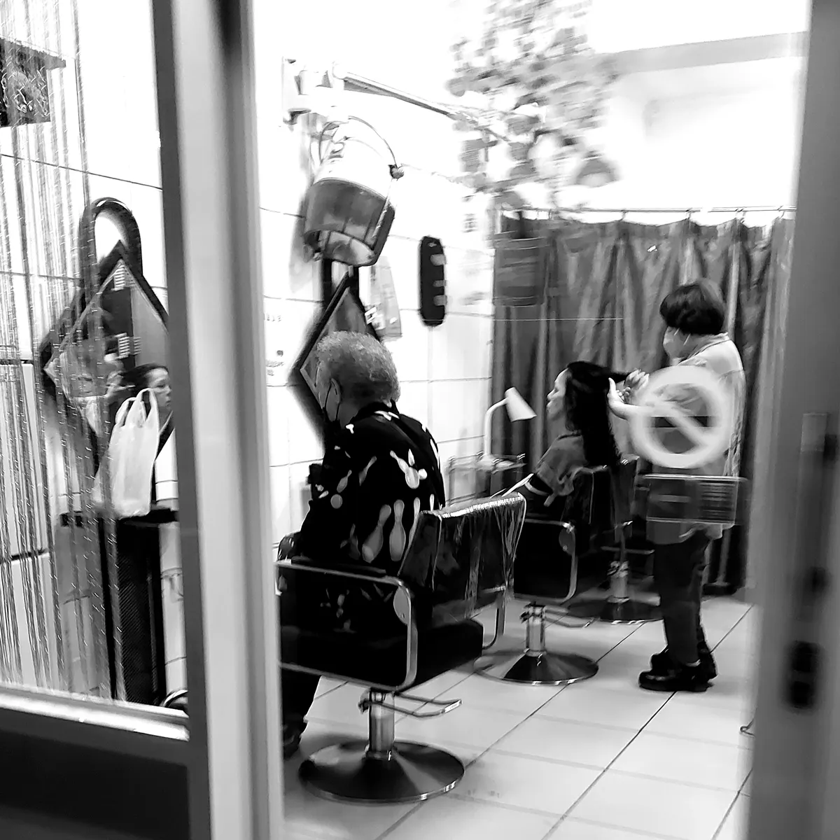 Hair salon: an old woman stares into a mirror while a young woman gets her hair cut beside her