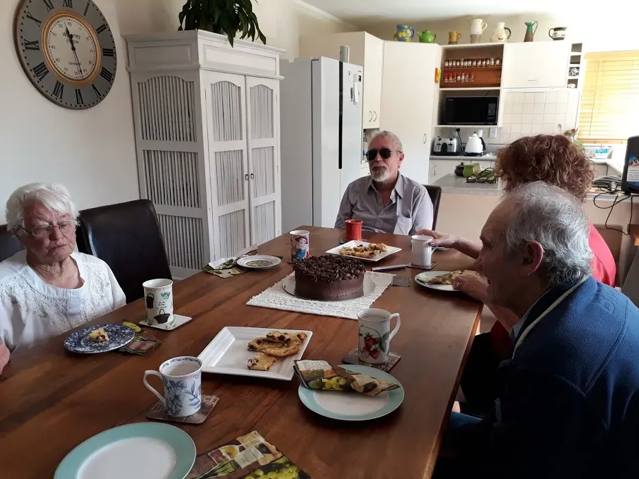 Blenheim deafblind network members sitting around a dining table sharing tea, cake and other refreshments.
