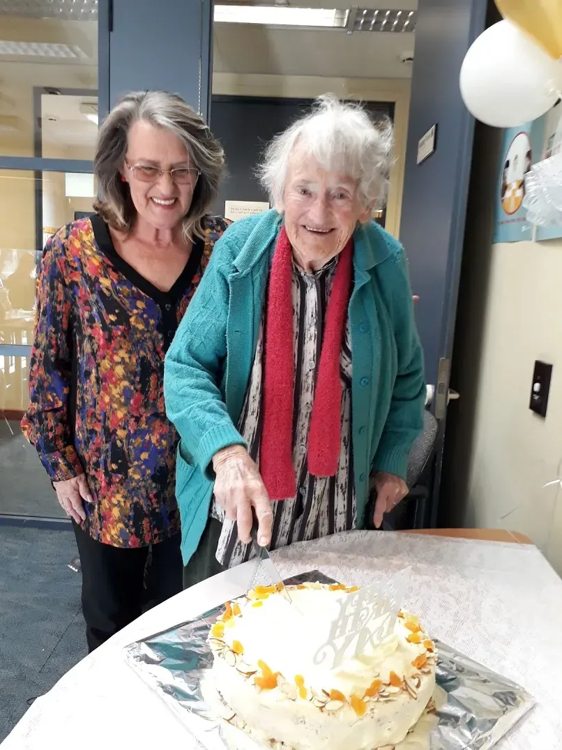 Kaye Ellison and member pointing to cake and smiling.