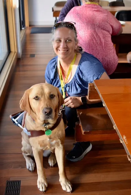 Sally Britnell smiling into the camera, crouched next to her guide dog, Sienna.