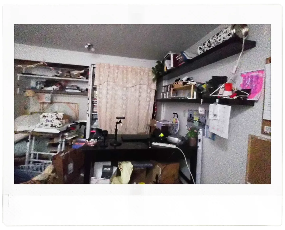 the same room, with much of the mess still there, but the desk is now rotated and its top is relatively clear with a laptop and camera set up