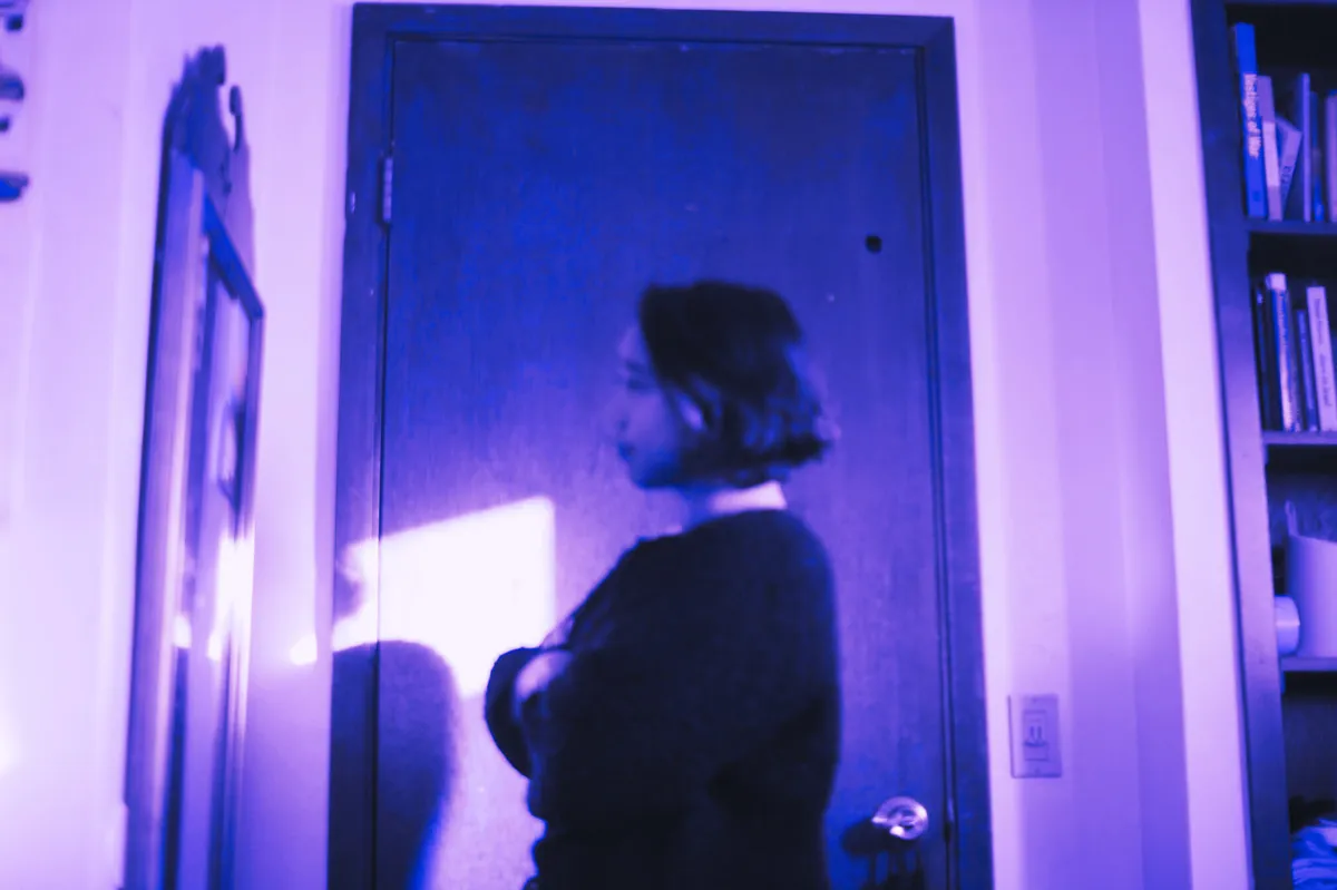 A purple tinted profile photo of Sarah Joy looking at a mirror