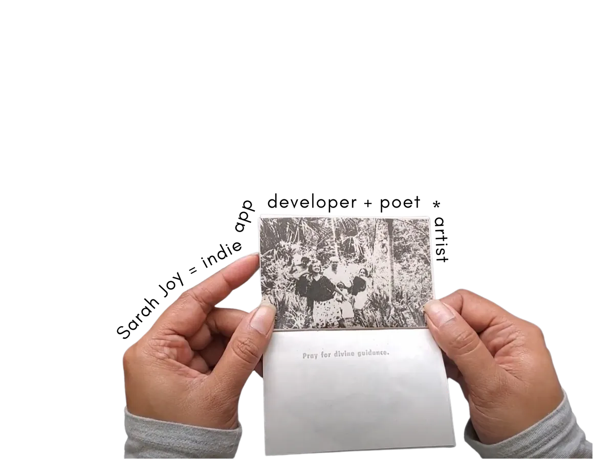 Sarah Joy holds up a zine with a photo of a a family walking through a jungle, an older woman raises her hand to her ear listening, and the text "pray for divine guidance" on the other side. Around her hands is text that says "Sarah Joy is an indie app developer + artist * poet