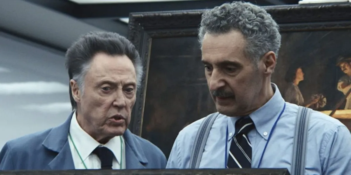 Recorte da série Ruptura. Na imagem, estão dois personagens, Burt e Irving. Burt é um homem branco mais velho, com algo entre 70 e 80 anos. Ele tem cabelo grisalho curto e penteado pra trás. Ele usa roupa social e um crachá. Na direita, olhando para baixo, está Irving, um homem marrom de uns 60 e poucos anos. Irving tem o cabelo levemente ondulado e curto, penteado pra trás. Ele usa bigode e também está de roupa social, mas sem o paletó. Atrás deles, é possível ver o pedaço de uma pintura de aspecto antigo, imitando uma reprodução renascentista.