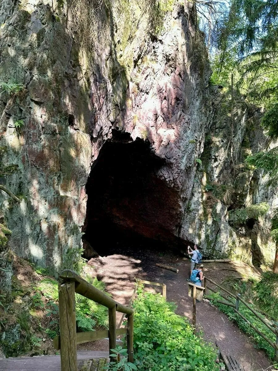 Das Backofenloch in Bad Tabarz. Ein großer Höhleneingang im Wald mit einer Person in der Nähe und umgeben von üppigem Grün.
