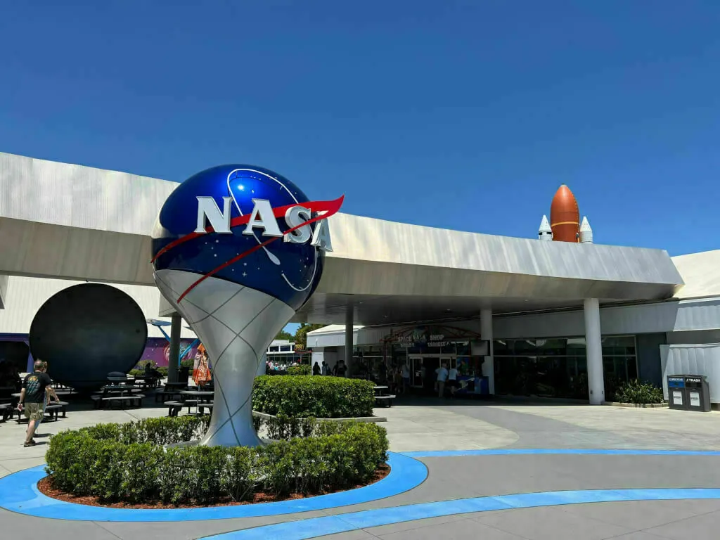 NASA-Logo im Kennedy Space Center in Florida. Im Hintergrund sieht man eine Saturn-Rakete.