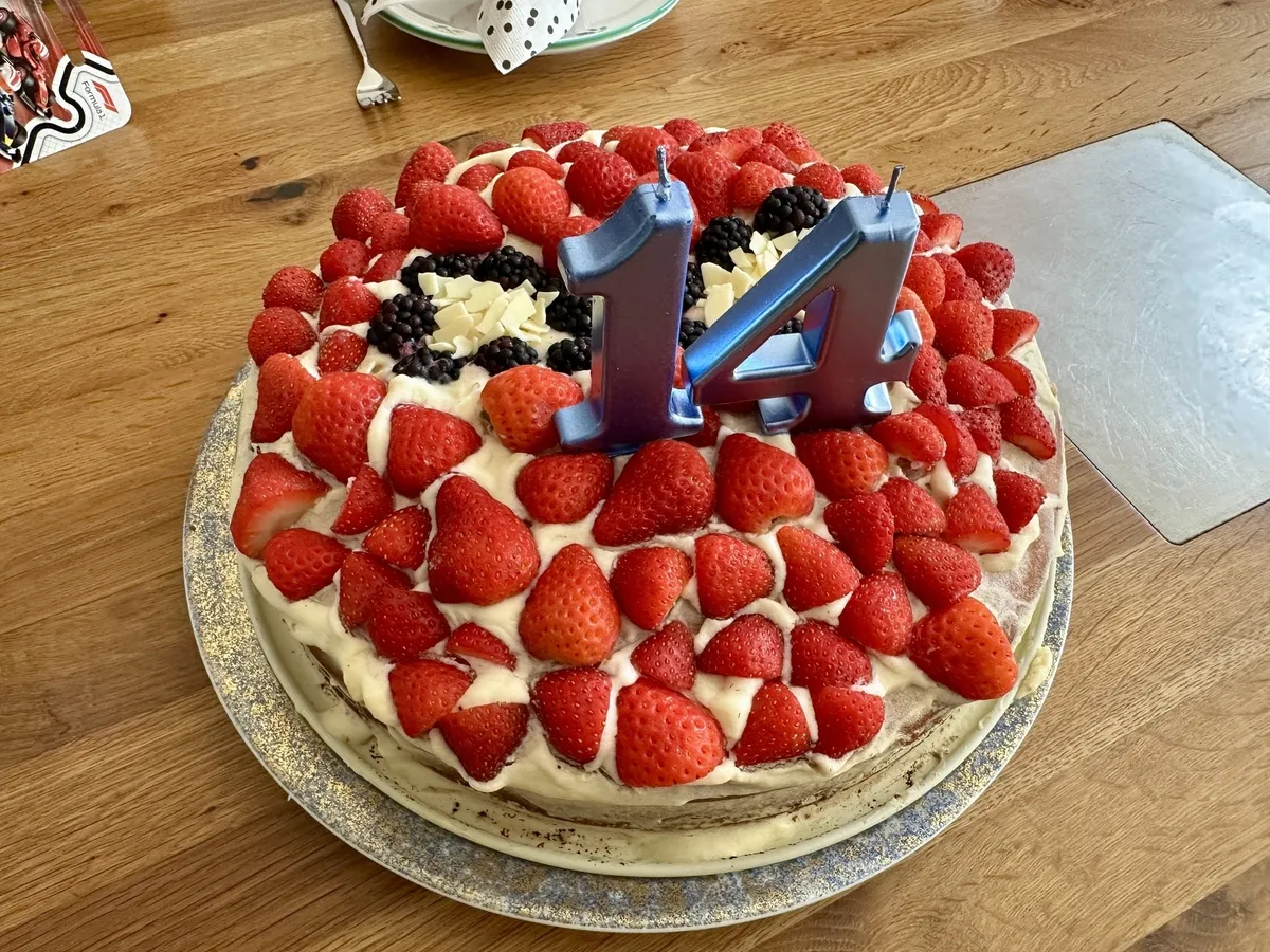Ein mit Erdbeeren und Sahne dekorierter Kuchen zeigt die Zahl 14 mit blauen Kerzen.