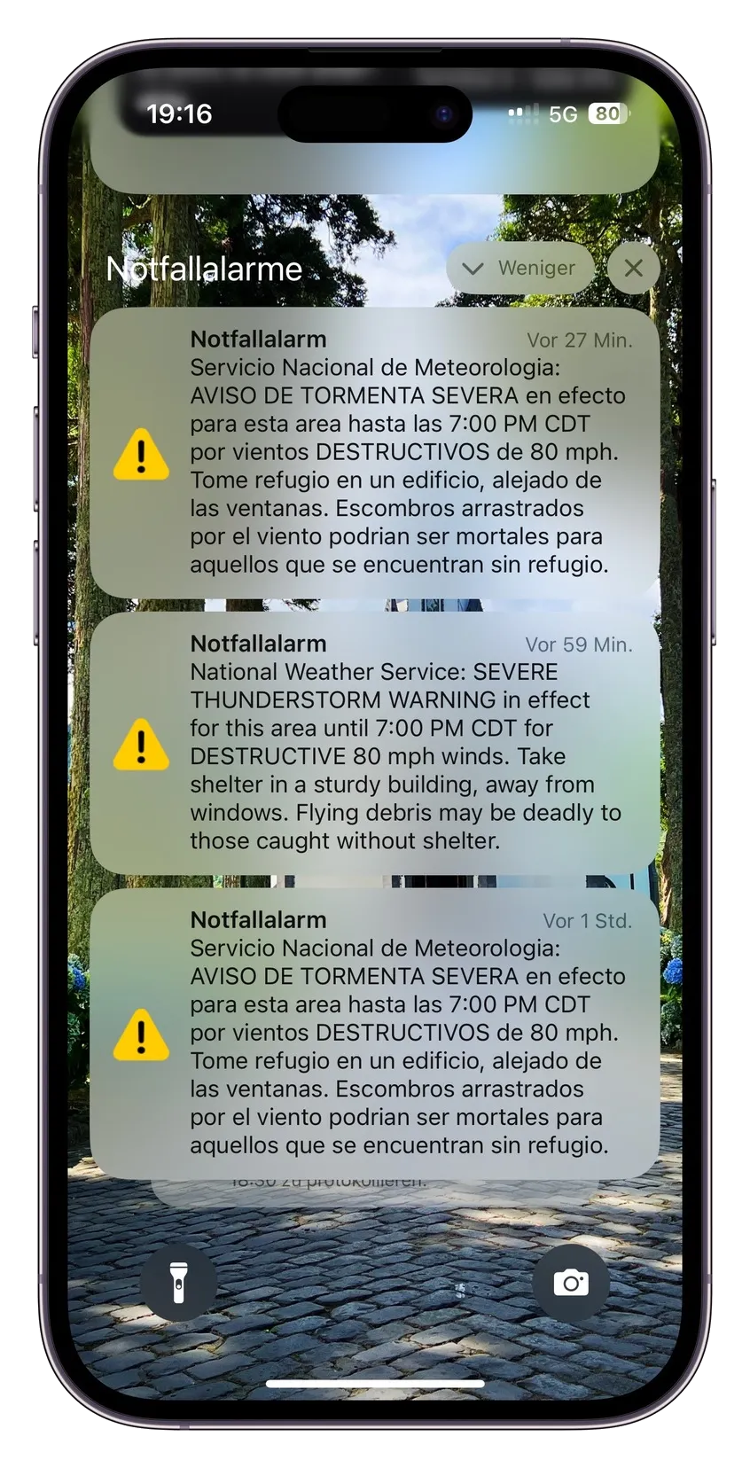 A smartphone screen displays severe thunderstorm warnings in multiple languages from the weather service, highlighting the risk of destructive winds.