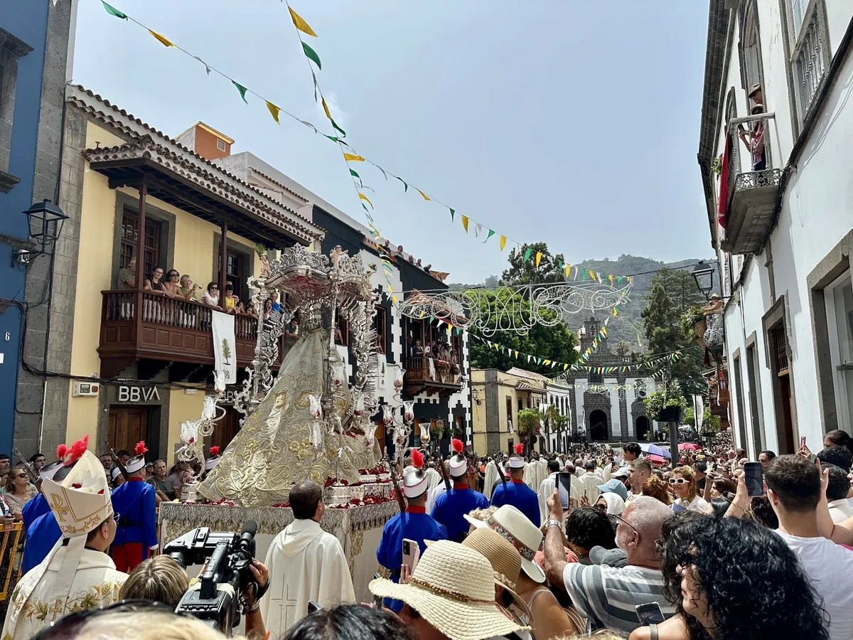 Eine Prozession zieht durch eine belebte Straße, begleitet von Zuschauern und geschmückten Gebäuden.