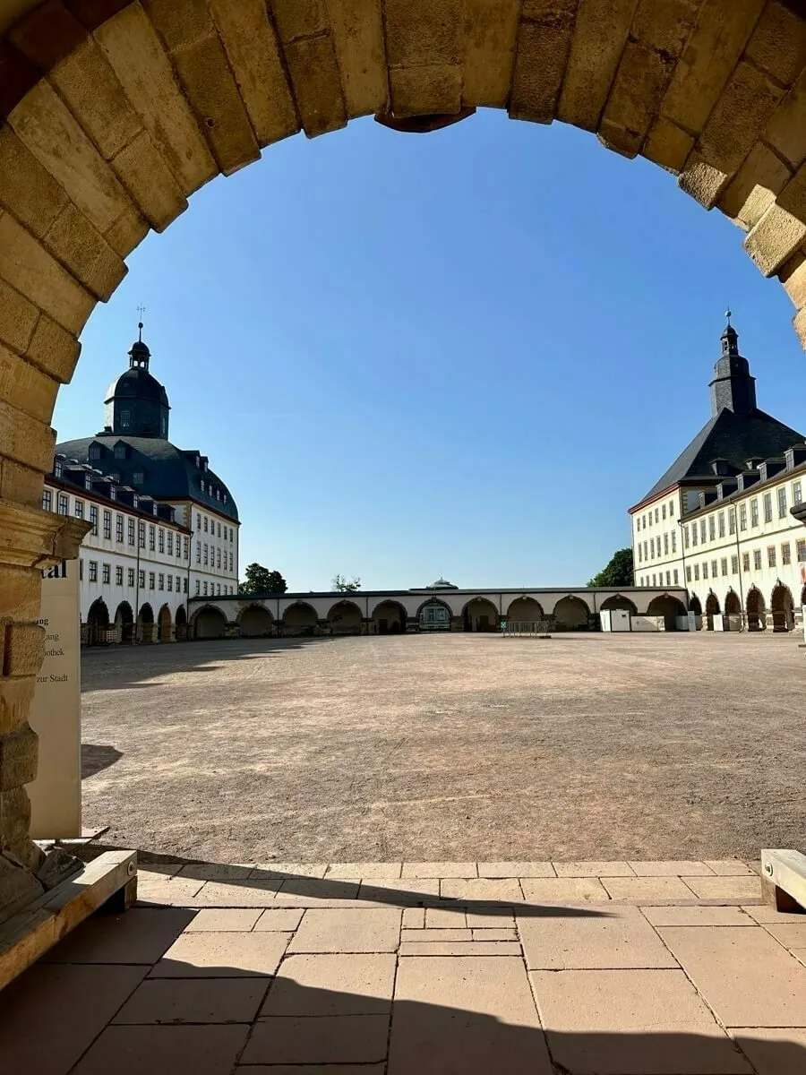 Der historische Innenhof vom Schloss Friedenstein mit den zwei unterschiedlichen Türmen im Hintergrund, eingerahmt von einem steinernen Torbogen.