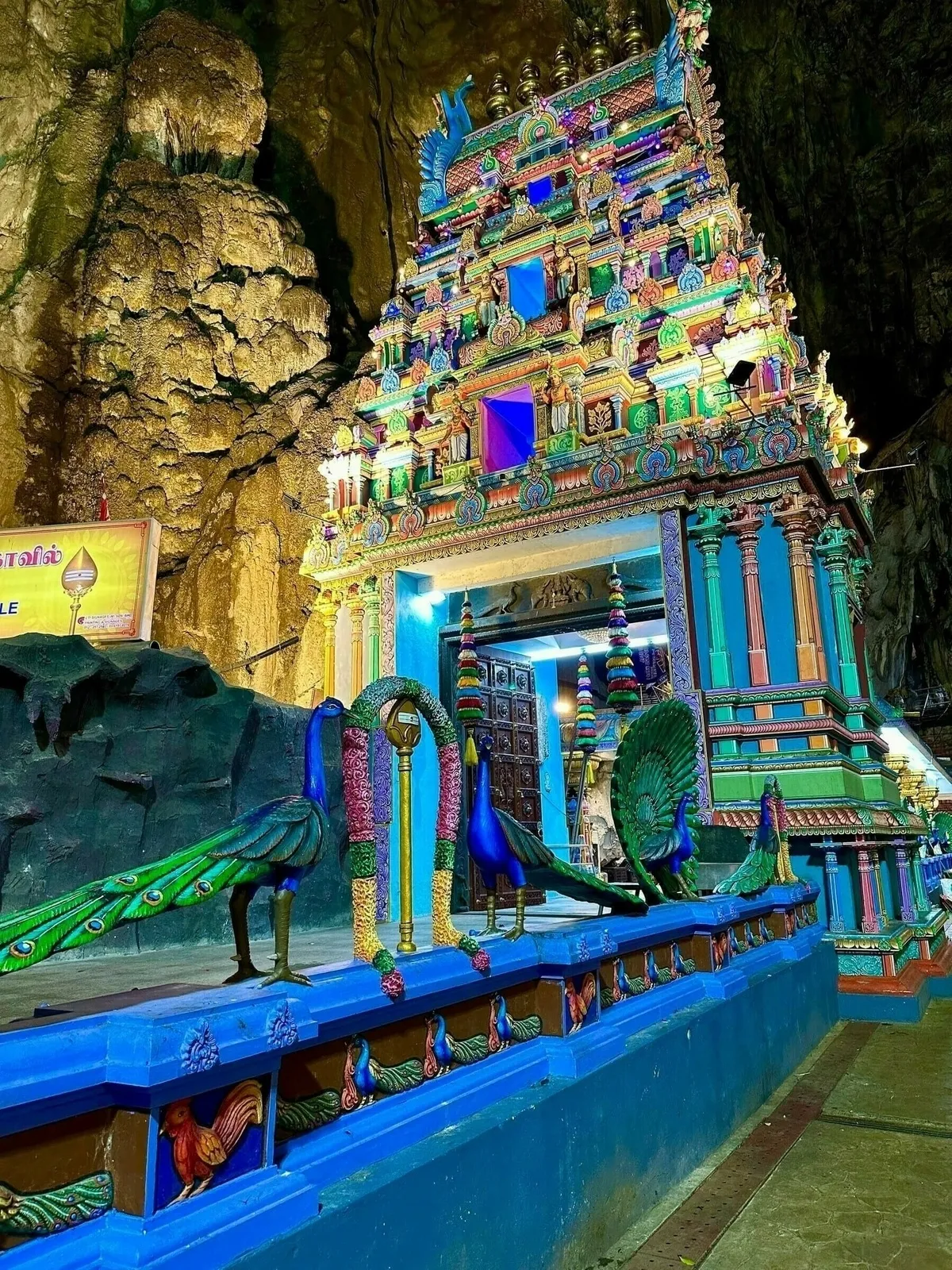 Ein Tempel in den Batu Caves, umgeben von hohen, moosbewachsenen Felsen.