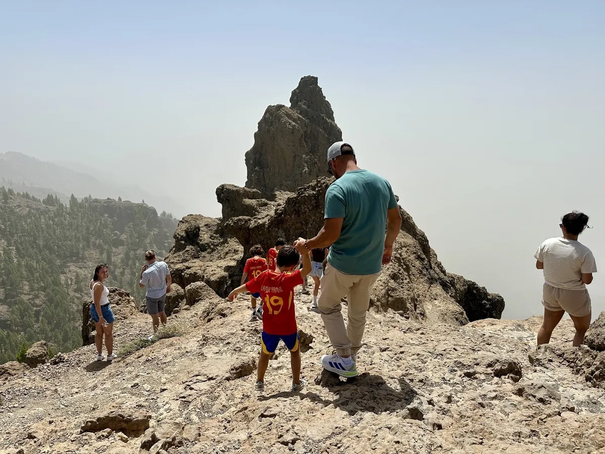 Eine Gruppe von Menschen steht auf dem Pico de las Nieves mit Bergen im Hintergrund.