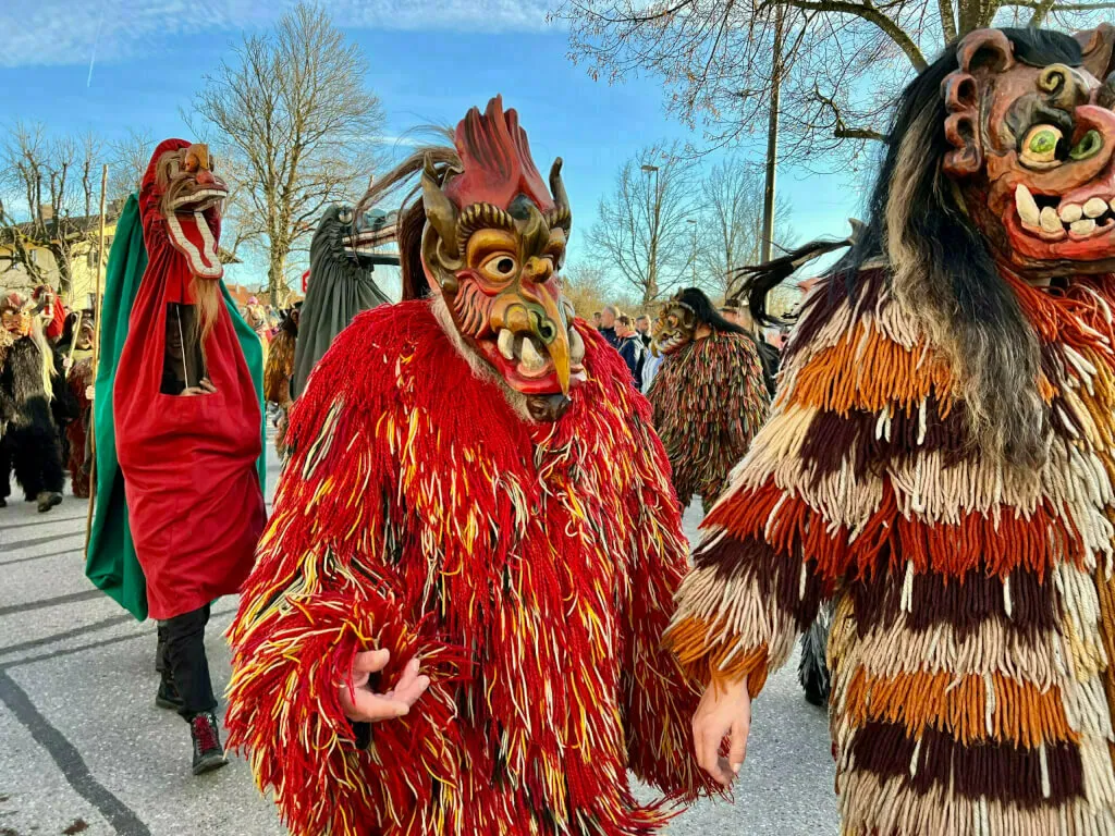Eine Gruppe von Personen in verschiedenen zotteligen, fellartigen Monster-Kostümen mit Tiermasken marschiert über eine Straße.