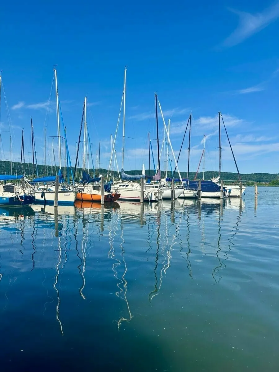 Segelboote liegen an einem Steg auf einem ruhigen See unter klarem, blauem Himmel.