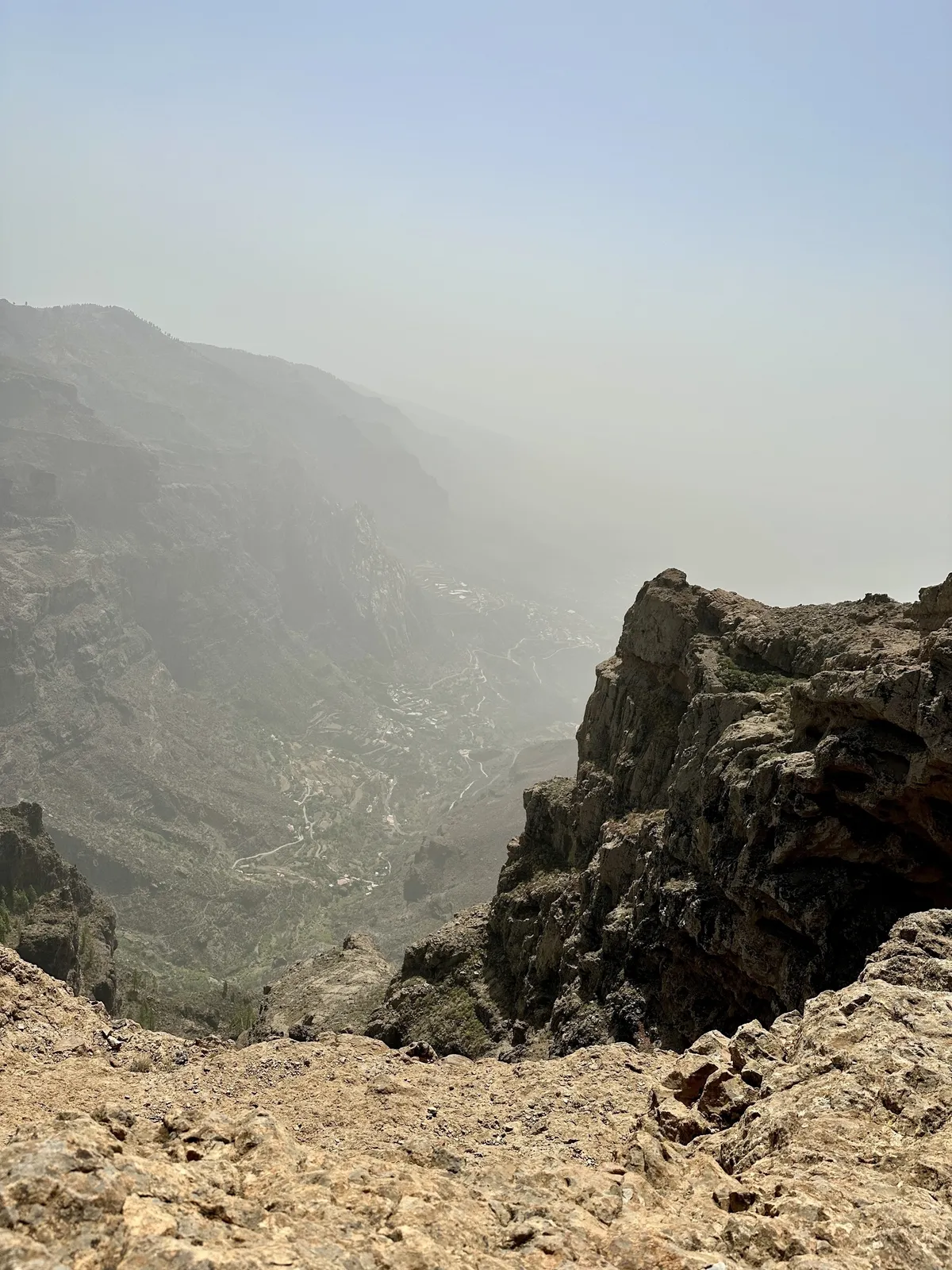 Ein felsiger Berghang mit einem nebligen Tal im Hintergrund.