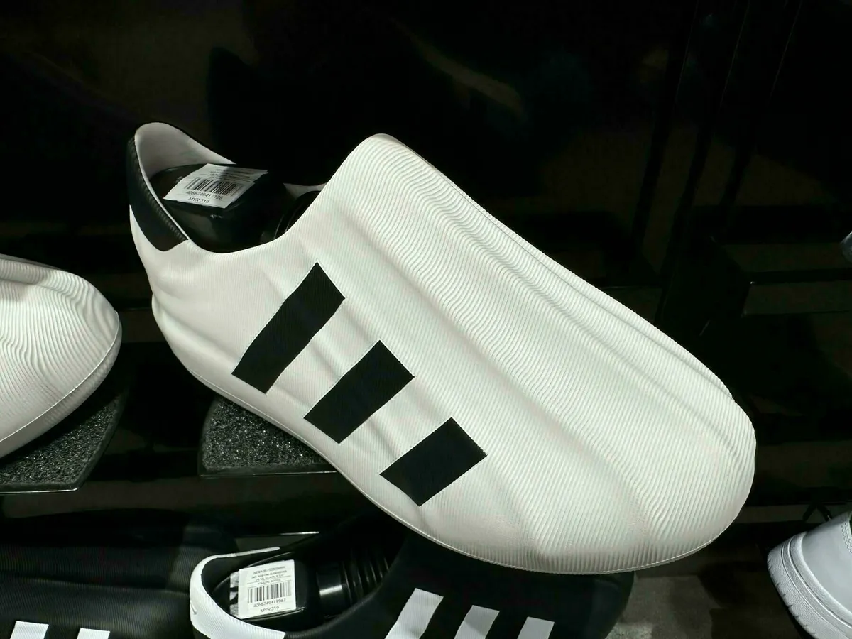 Ein Paar futuristisch aussehende, weiße Badelatschen oder Slides mit den drei schwarzen Adidas-Streifen an der Seite, die in einem Geschäft ausgestellt sind.