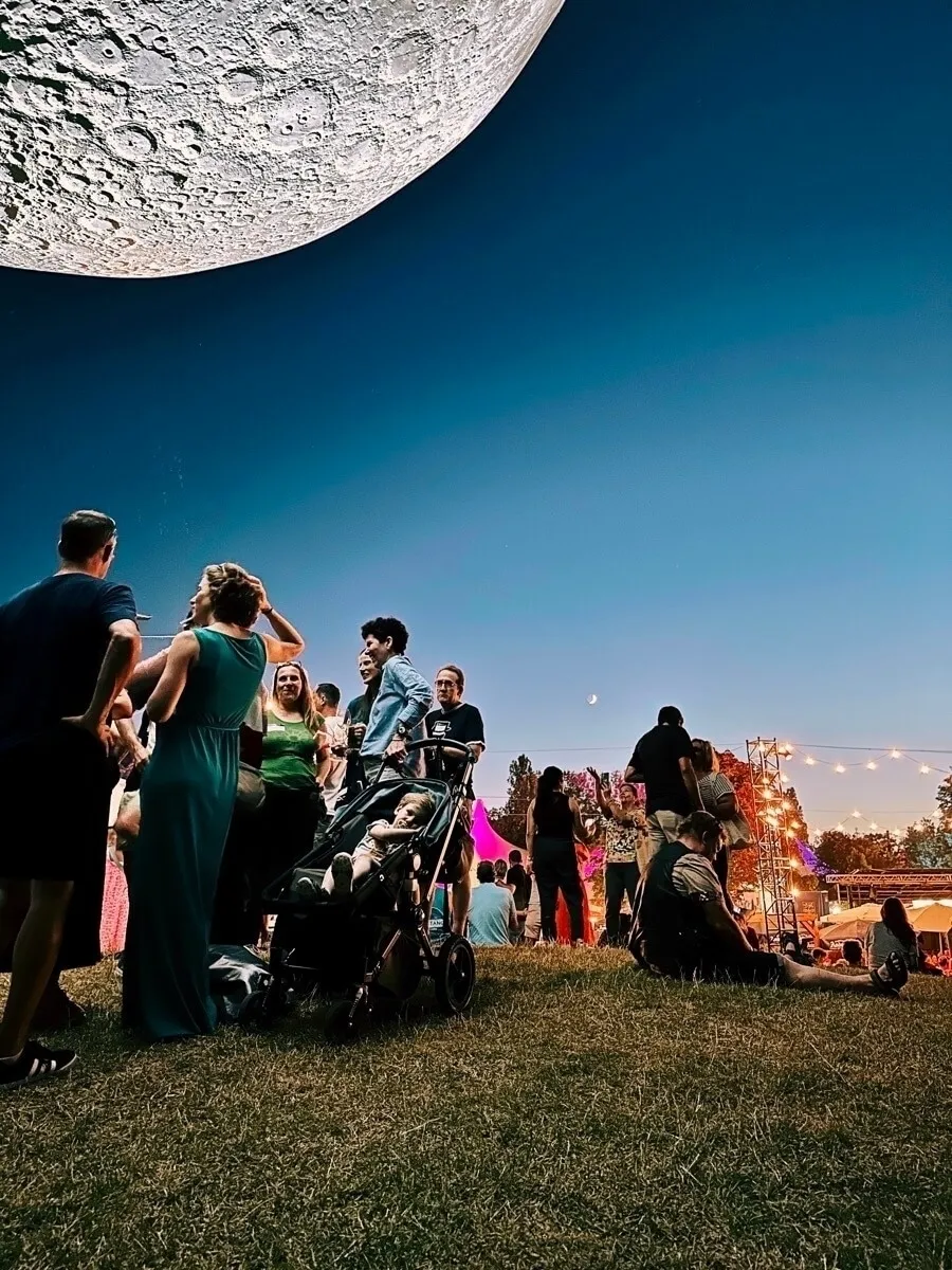 Eine Gruppe von Menschen genießt ein Fest im Freien, während ein riesiger Mond am Himmel zu sehen ist.