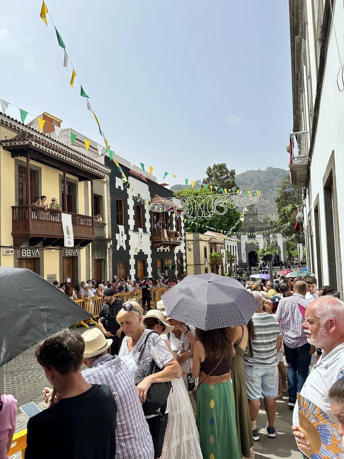 Eine Menschenmenge versammelt sich auf einer belebten Straße in einer spanischen Stadt, die mit bunten Wimpeln und typischen kanarischen Balkonen geschmückt ist.