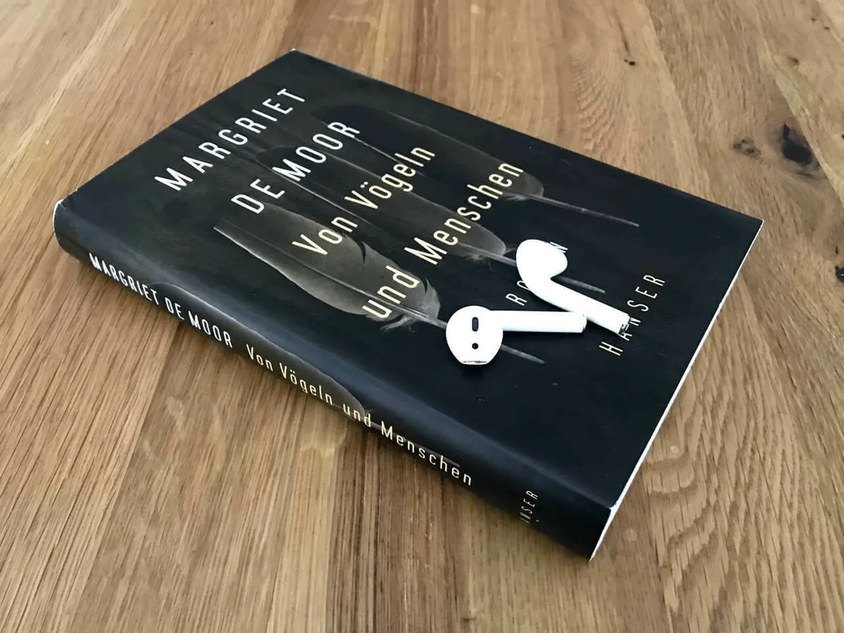 Das Buch "Von Vögeln und Menschen" mit einem Paar Apple Airpods