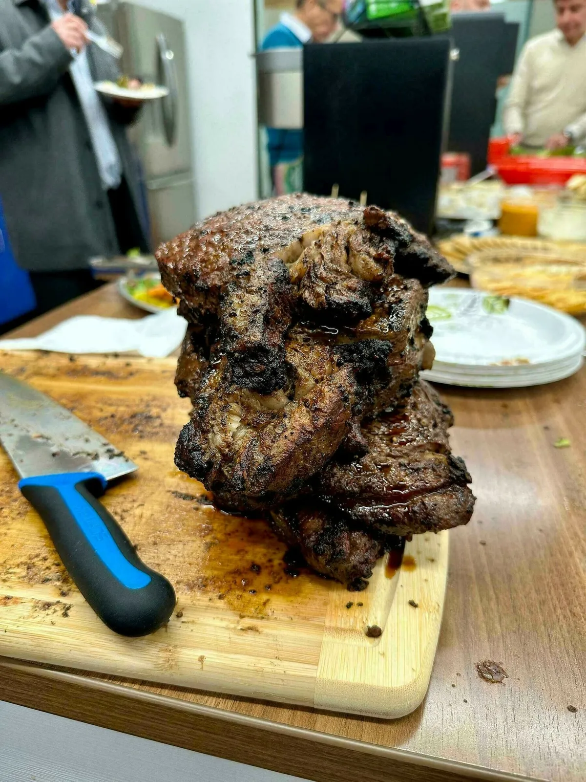 Mehrere gebratene Steaks liegen gestapelt auf einem hölzernen Schneidebrett, umgeben von Tellern, wobei ein Messer in der Nähe ruht.