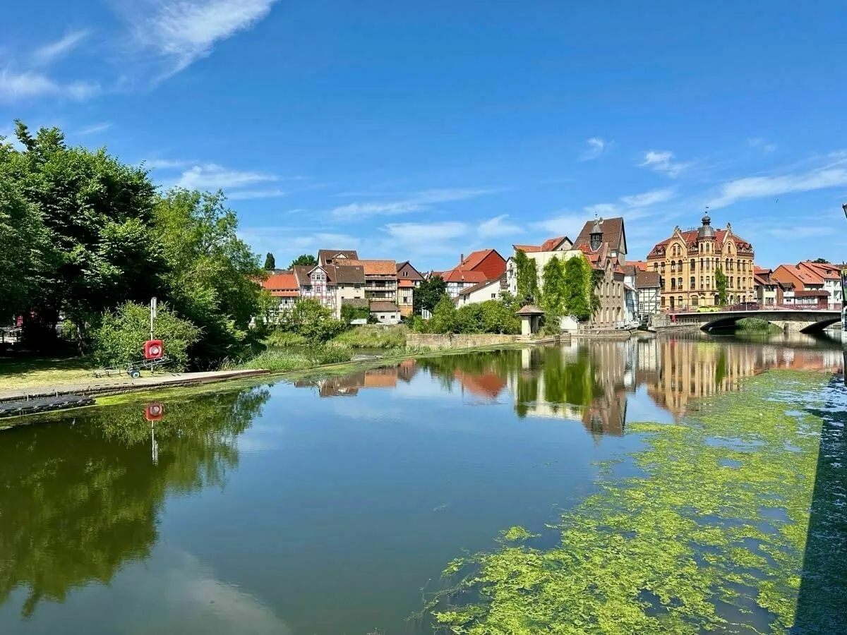Eine malerische Flusslandschaft mit historischen Gebäuden am Ufer und einer Brücke unter klarem blauem Himmel.