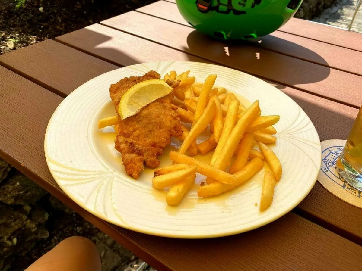 Ein großer Teller mit einem knusprigen Schnitzel und einer Zitrone sowie einer reichlichen Portion goldgelber Pommes frites auf einem Holztisch.