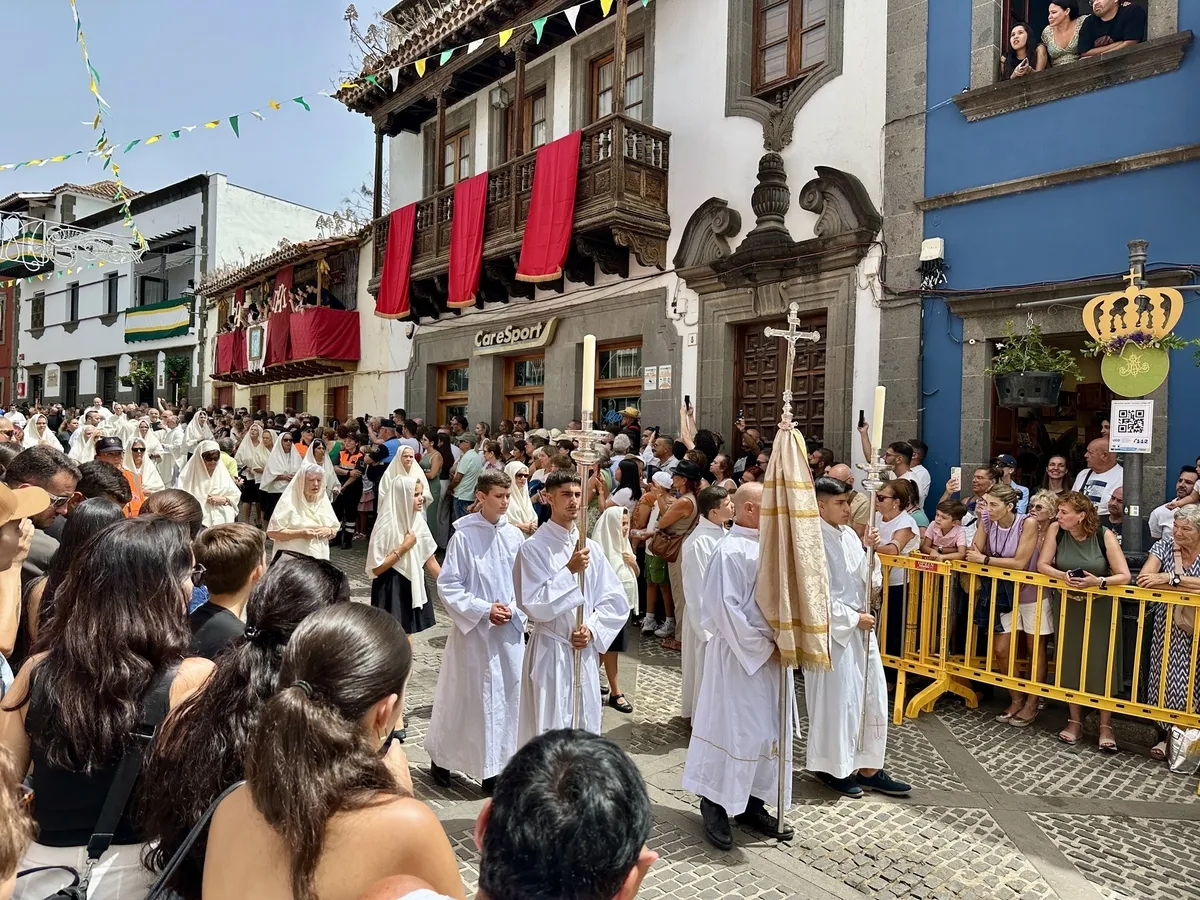 Menschen in weißen Gewändern nehmen an einer religiösen Prozession auf einer belebten Straße mit Zuschauern und geschmückten Gebäuden teil.