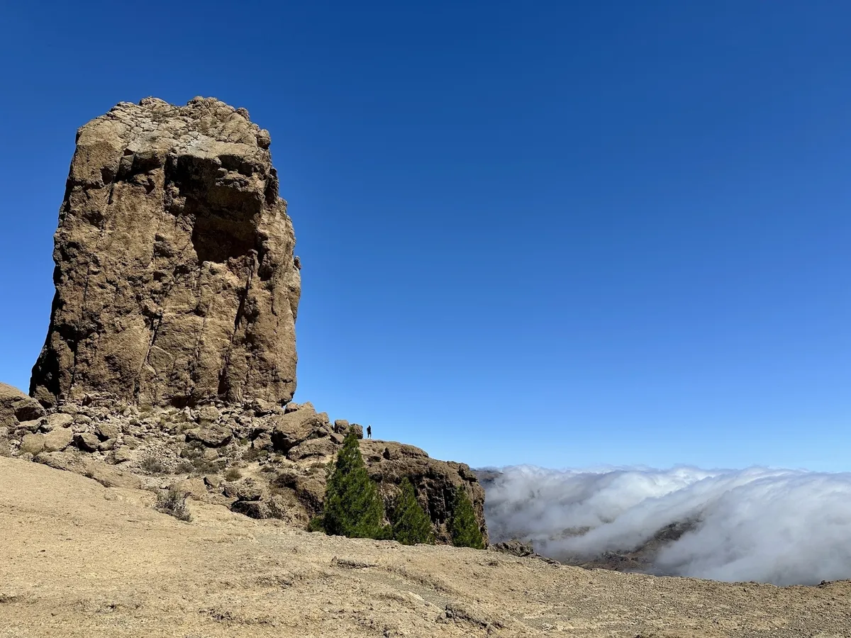 Der Roque Nublo erhebt sich über die karge Landschaft von Gran Canaria, während sich am Horizont eine Wolkendecke erstreckt.