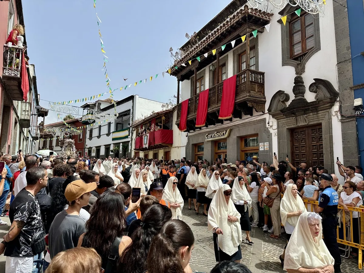 Menschen nehmen in traditioneller Kleidung an einer Prozession in einer belebten, mit Fahnen dekorierten Straße teil.