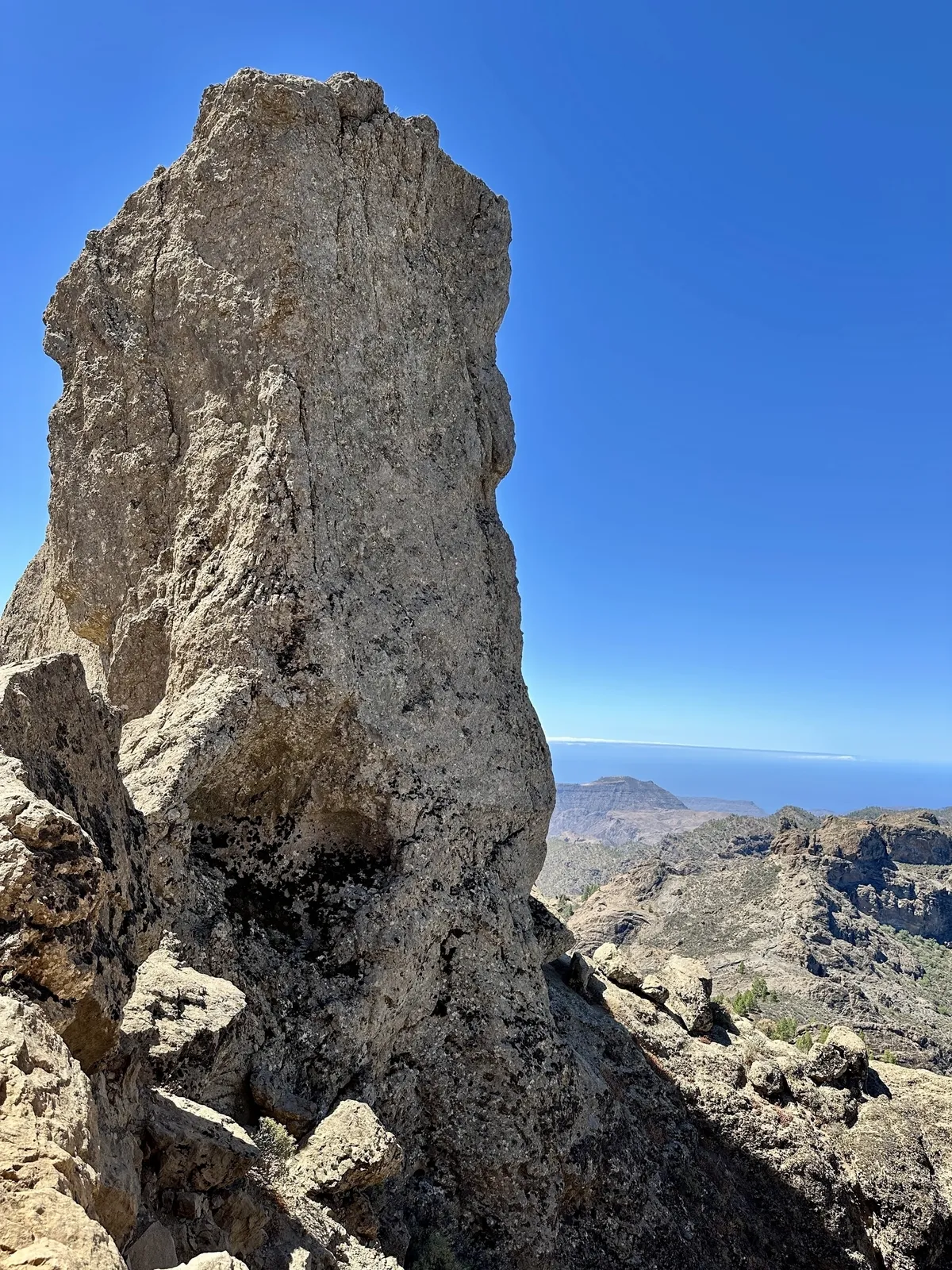Der Roque Nublo erhebt sich beeindruckend vor einem klaren blauen Himmel in einer felsigen Berglandschaft.